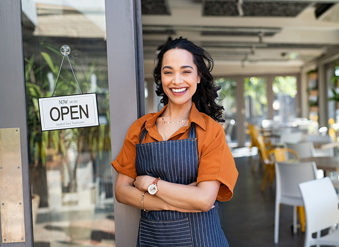 Business Insurance - Portrait of a Cheerful Young Female Business Owner Standing Next to the Front Door of her Cafe with an Open Sign
