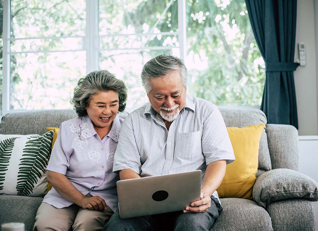 General Medicare - Senior Couple Laughing While Sitting on the Sofa and Using Laptop to Review Their Medicare Options